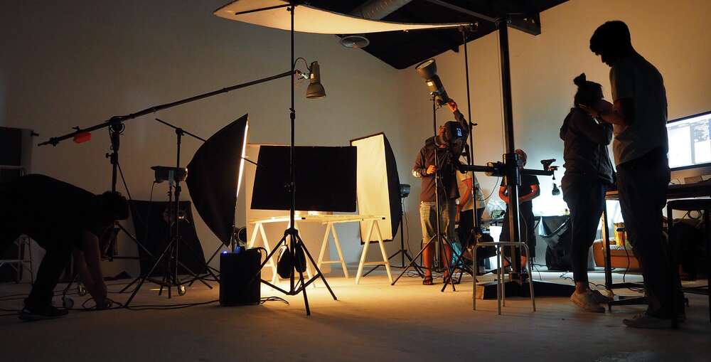 Silhouette view of people working in a photography studio with equipment, lights, and a table.